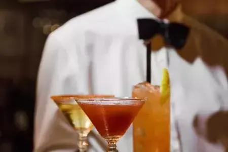 A server wearing a bowtie presents a tray of cocktails at Absinthe Restaurant in San Francisco.